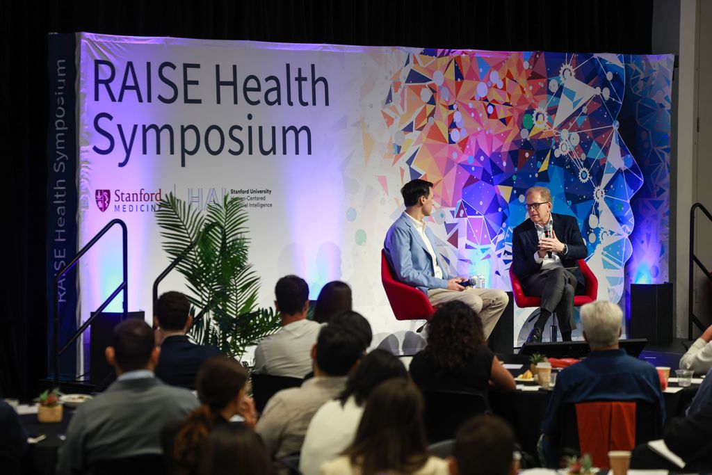 Two speakers discuss topics on stage at the RAISE Health Symposium.