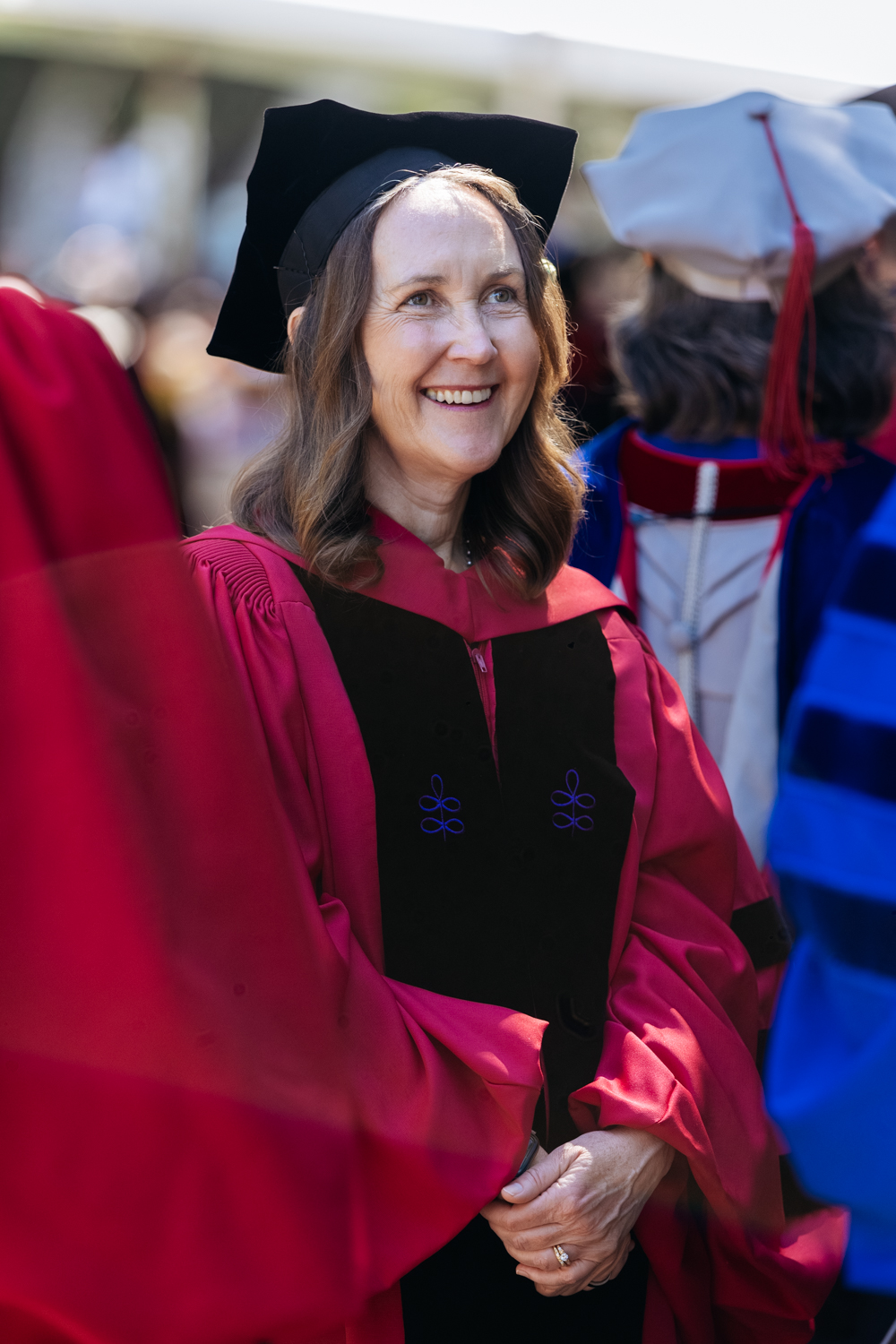 Provost Jenny Martinez in a red graduation gown and cap stands among others at a commencement ceremony.