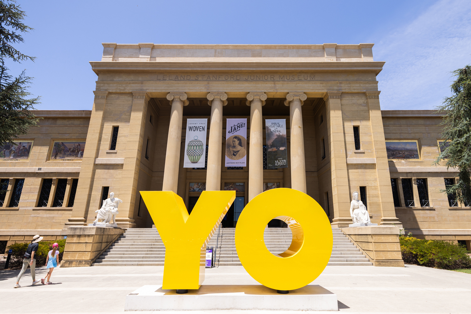 Two visitors walk past a giant yellow 