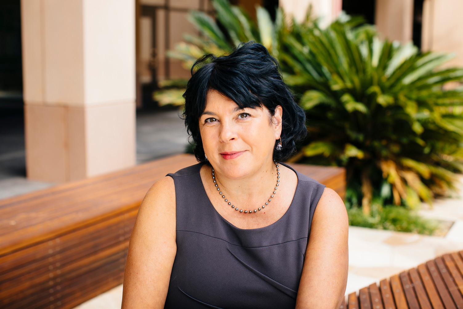 Michele Gelfand posing for a photo while sitting on a wood bench outdoors.