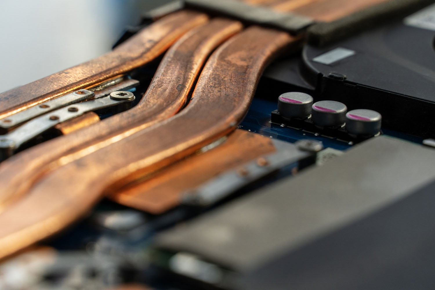 Macro shot of copper heat pipes on a laptop's circuit board, with capacitors and screws visible, shallow depth of field.