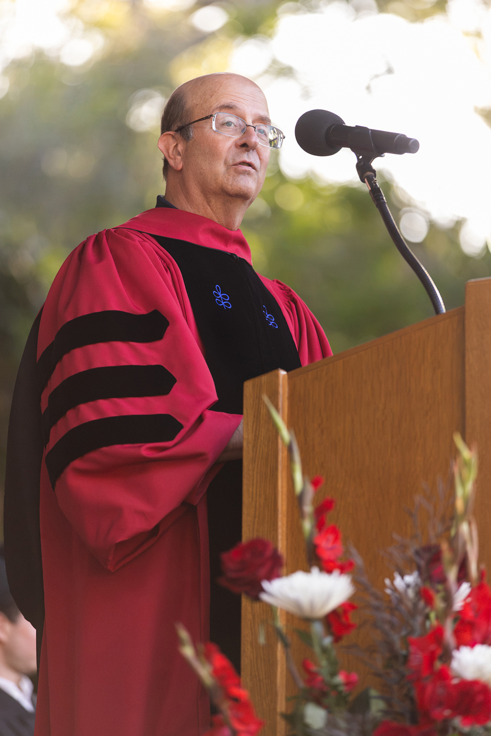 Vice Provost for Undergraduate Education Jay Hamilton in red academic regalia addresses the crowd from a podium.