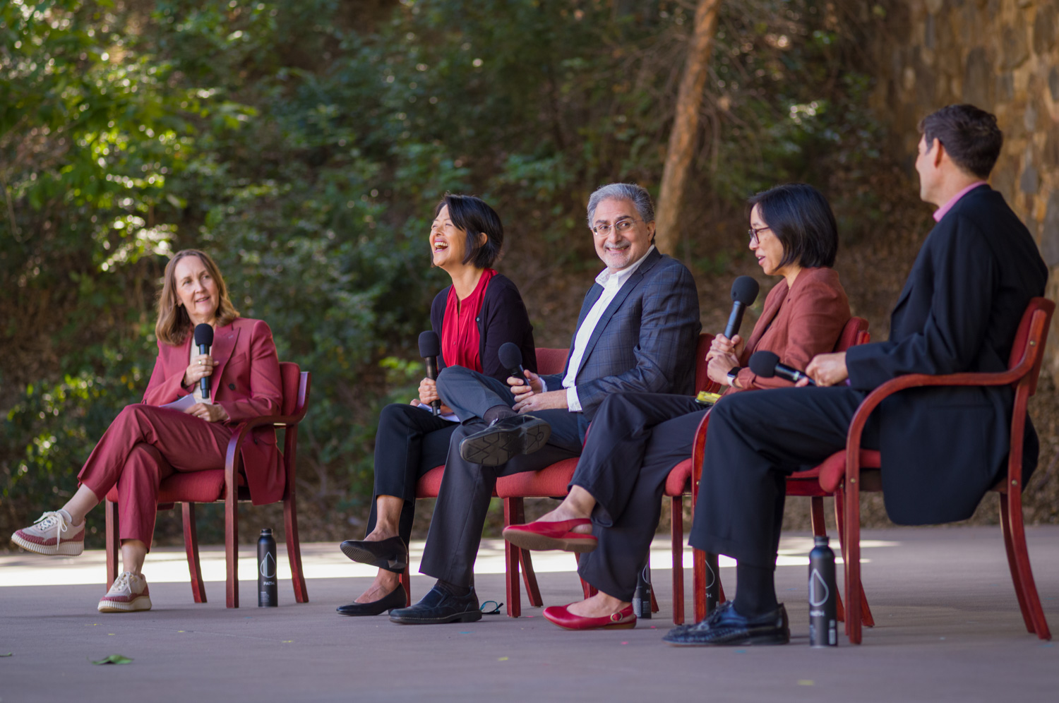 Stanford faculty members sit for a panel discussion, laughing together while holding microphones outdoors.