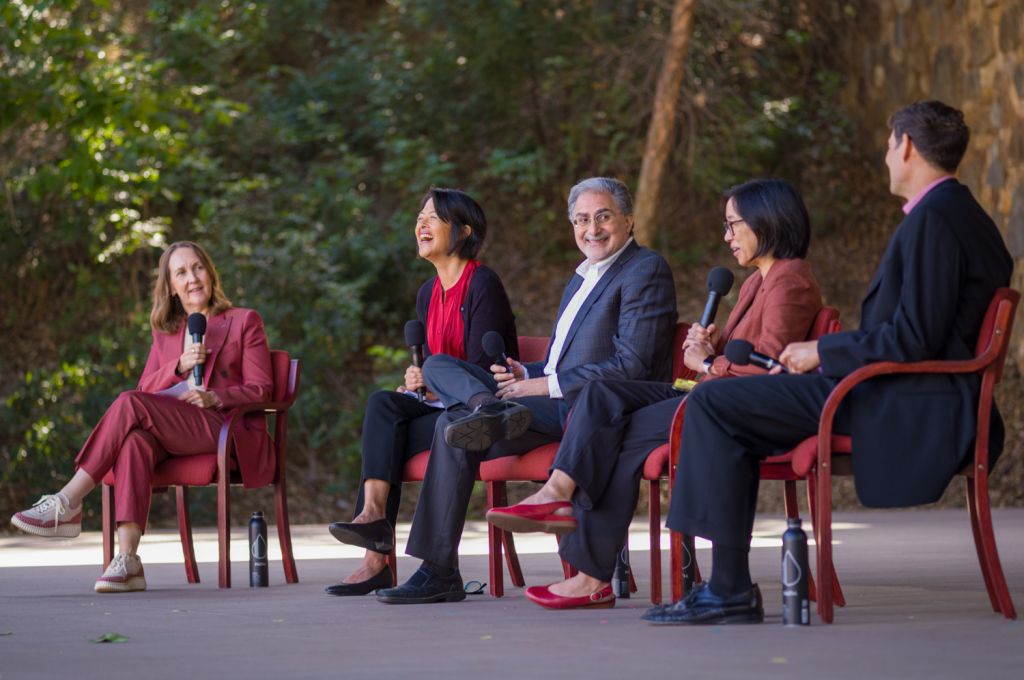 Stanford faculty members sit for a panel discussion, laughing together while holding microphones outdoors.