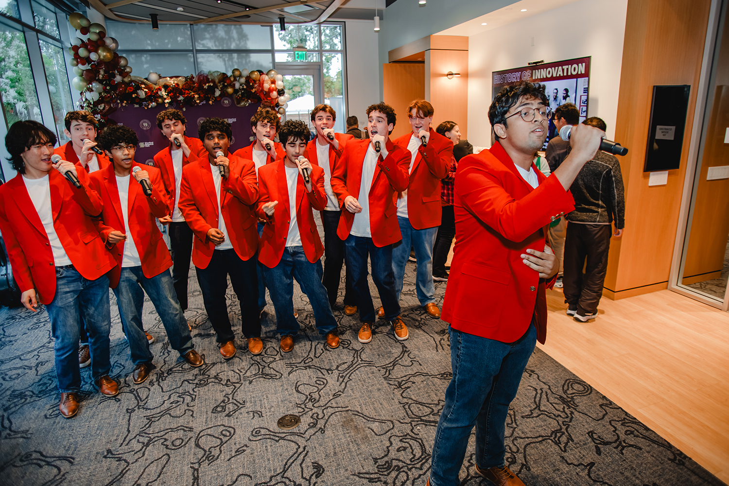A cappella singers The Mendicants in matching red blazers and jeans perform with microphones at the celebration.