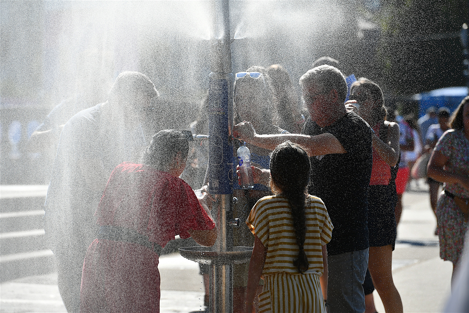 People stand in the spray of a water dispenser in a city