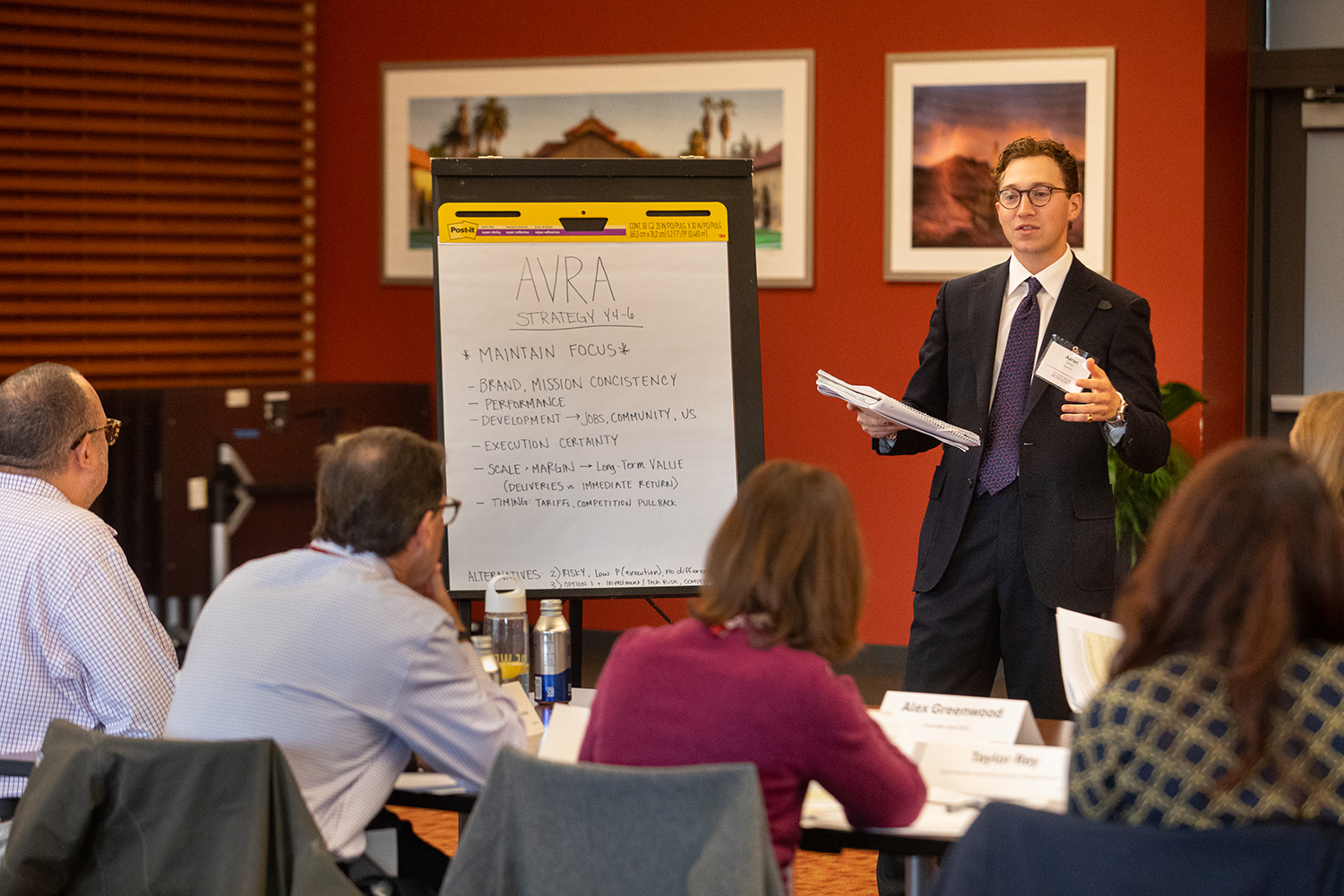 A facilitator presents strategy points on a flip chart during a workshop, while participants attentively engage in the discussion.