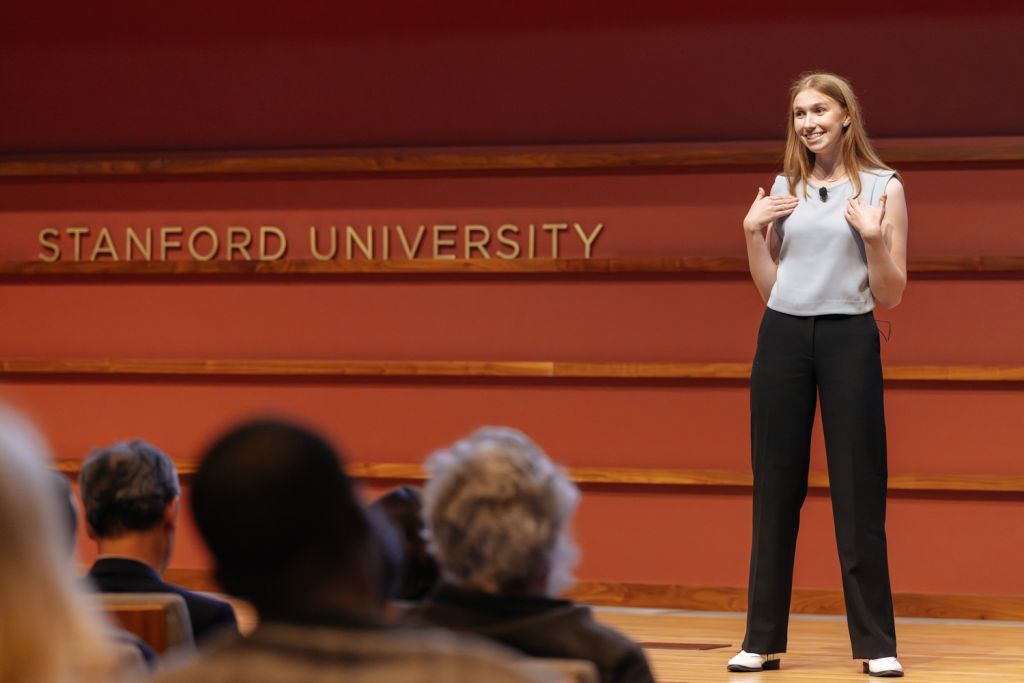 Colette Benko presenting on stage at 3MT competition.