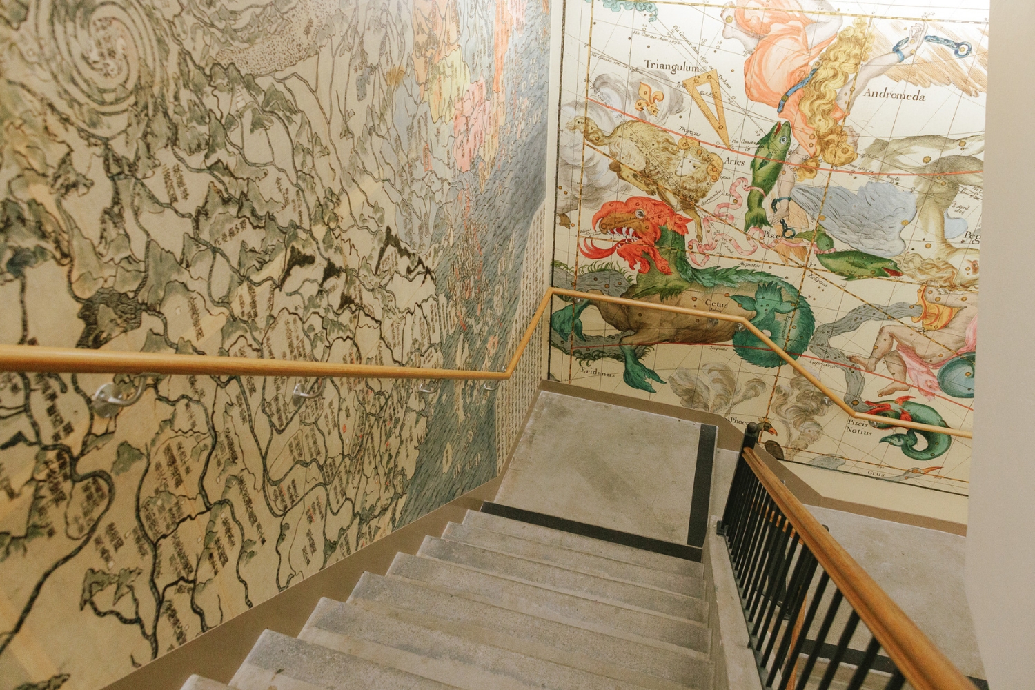 A staircase leads down past colorful, detailed wall murals depicting maps and mythical creatures.