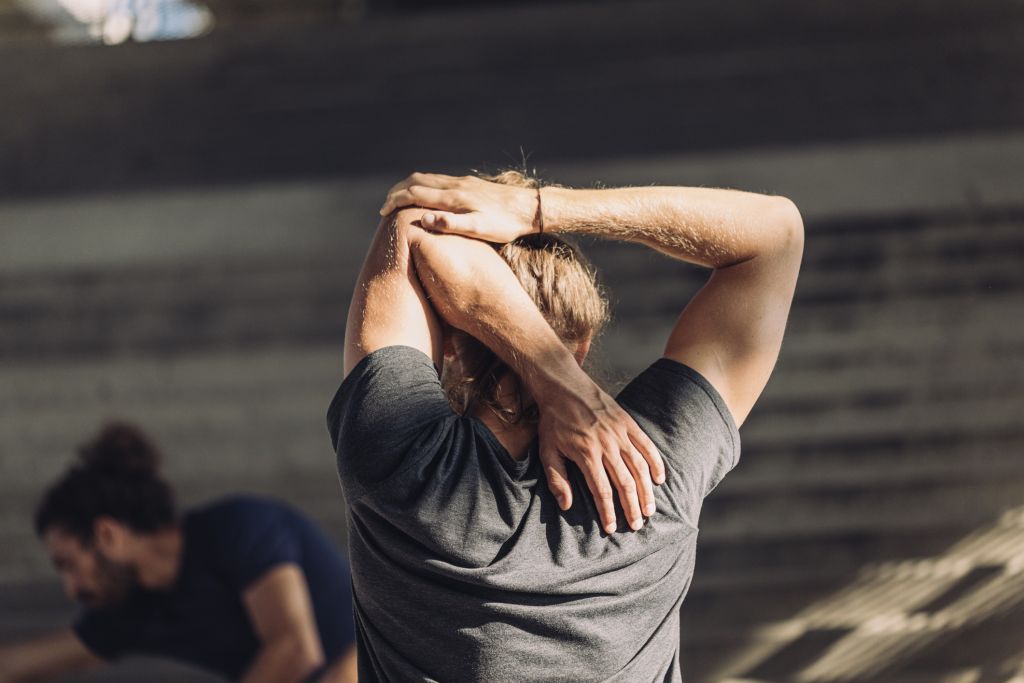 Photo of a man from behind stretching his arm muscles