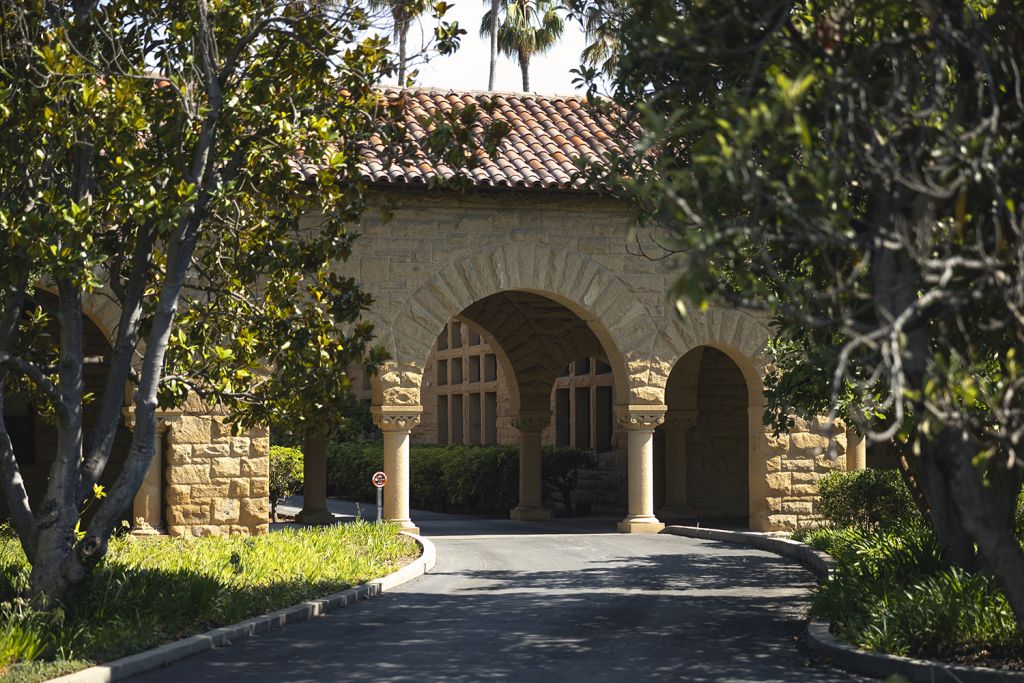 Path through stone archway with red tile roof surrounded by trees on a sunny day.