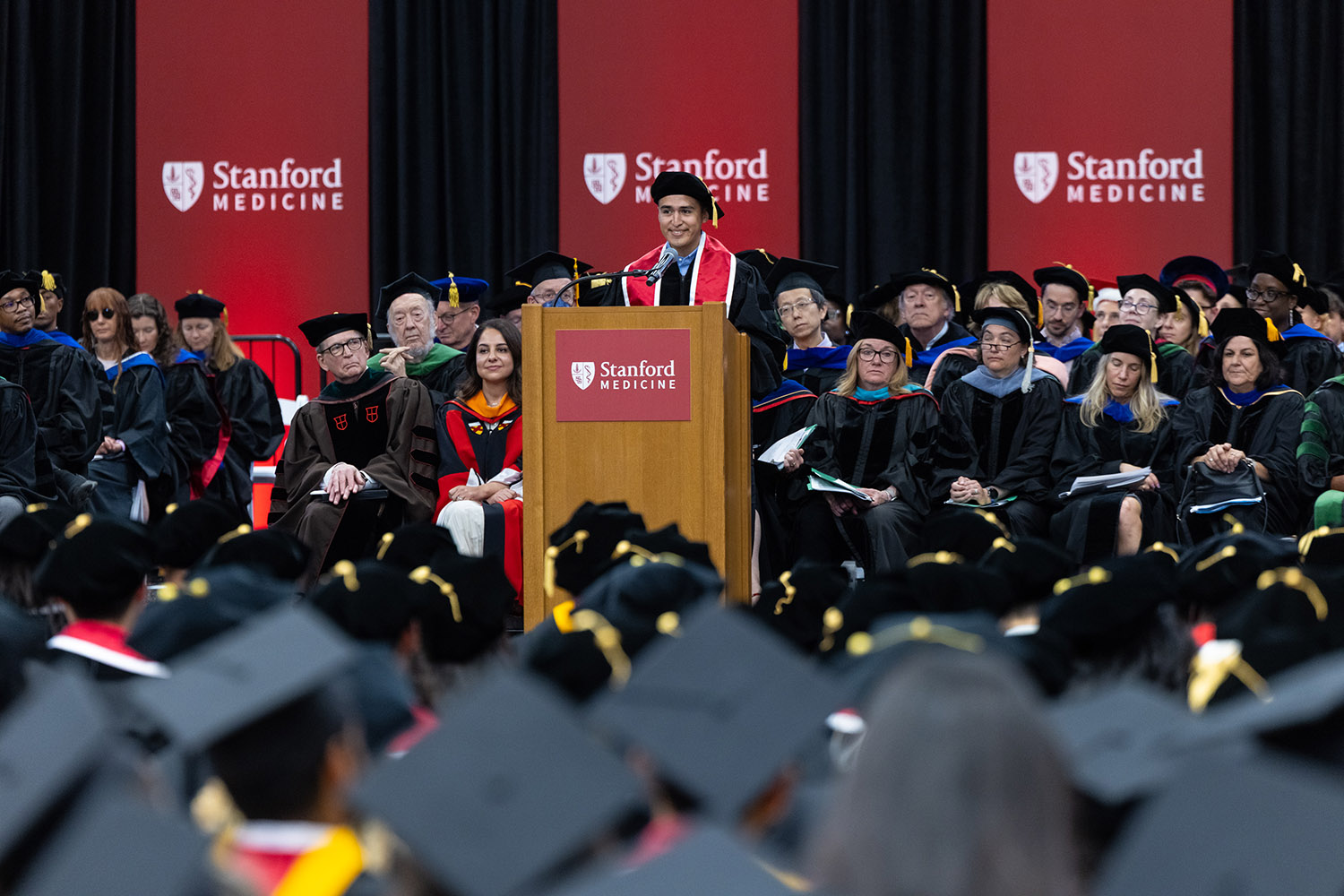 Speaker in academic regalia addresses graduates and faculty at Stanford Medicine commencement ceremony.