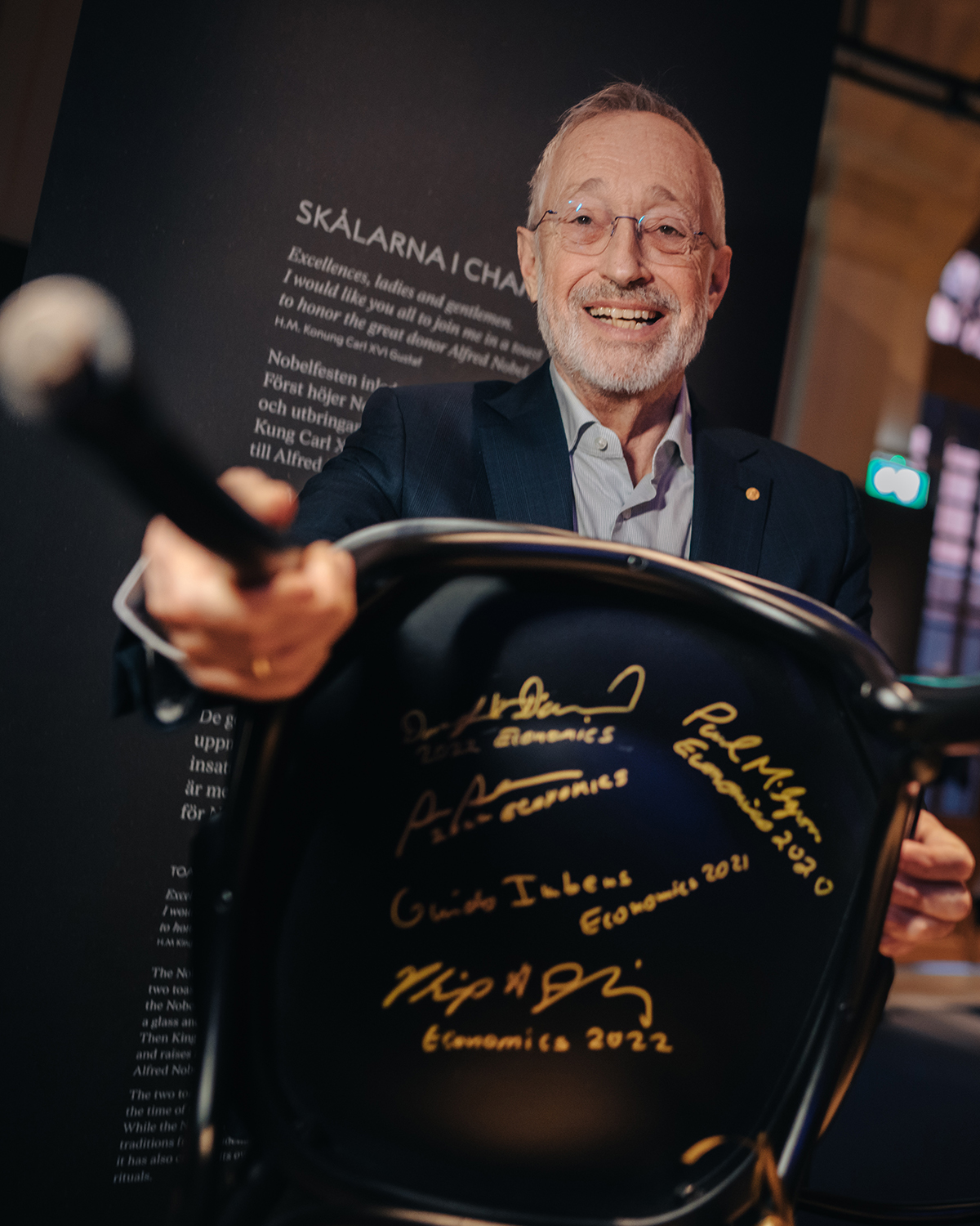 Paul Milgrom holds out a chair signed in gold by Nobel economics laureates from 2020 to 2022.