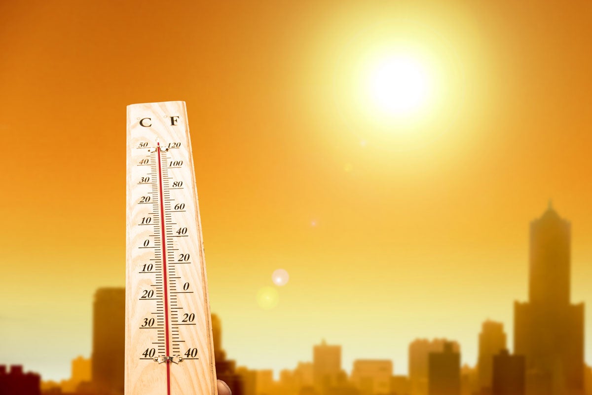 thermometer in foreground and city skyline in background under a blazing sun