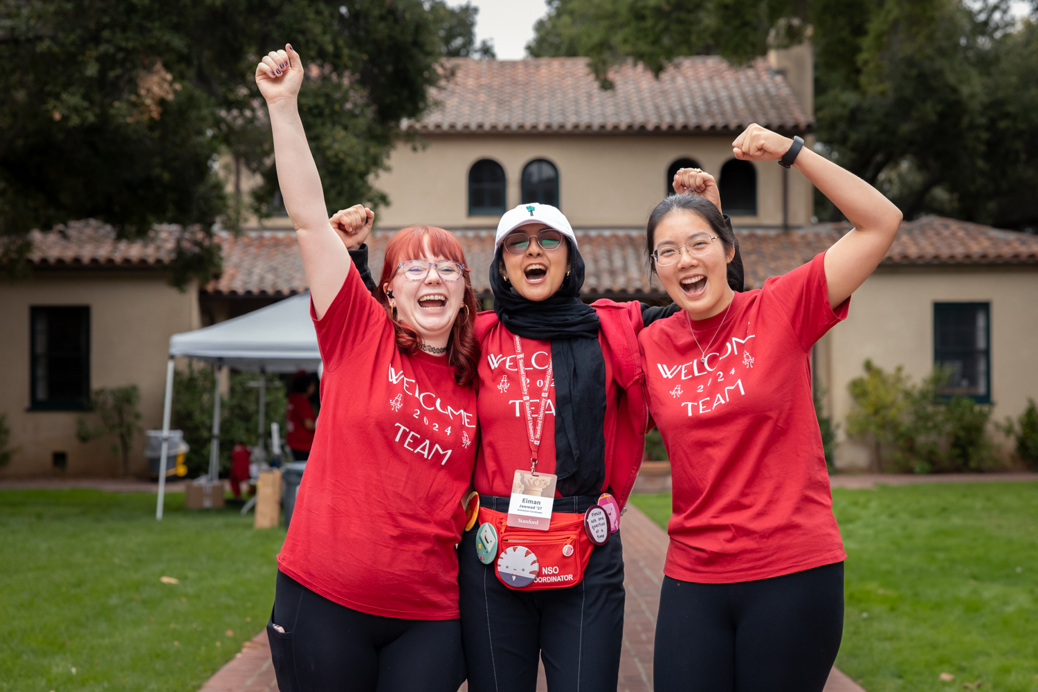 Three enthusiastic students wearing Welcome Team 2024 shirts cheer together.