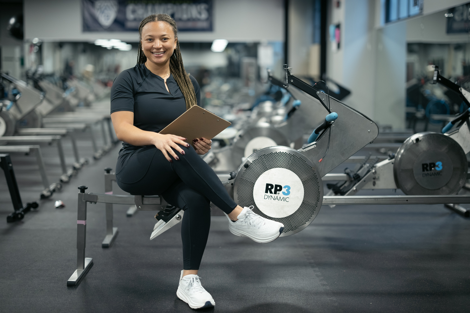 Postdoctoral scholar Morgan Smith poses for a picture while sitting on a bench in a gym on campus.
