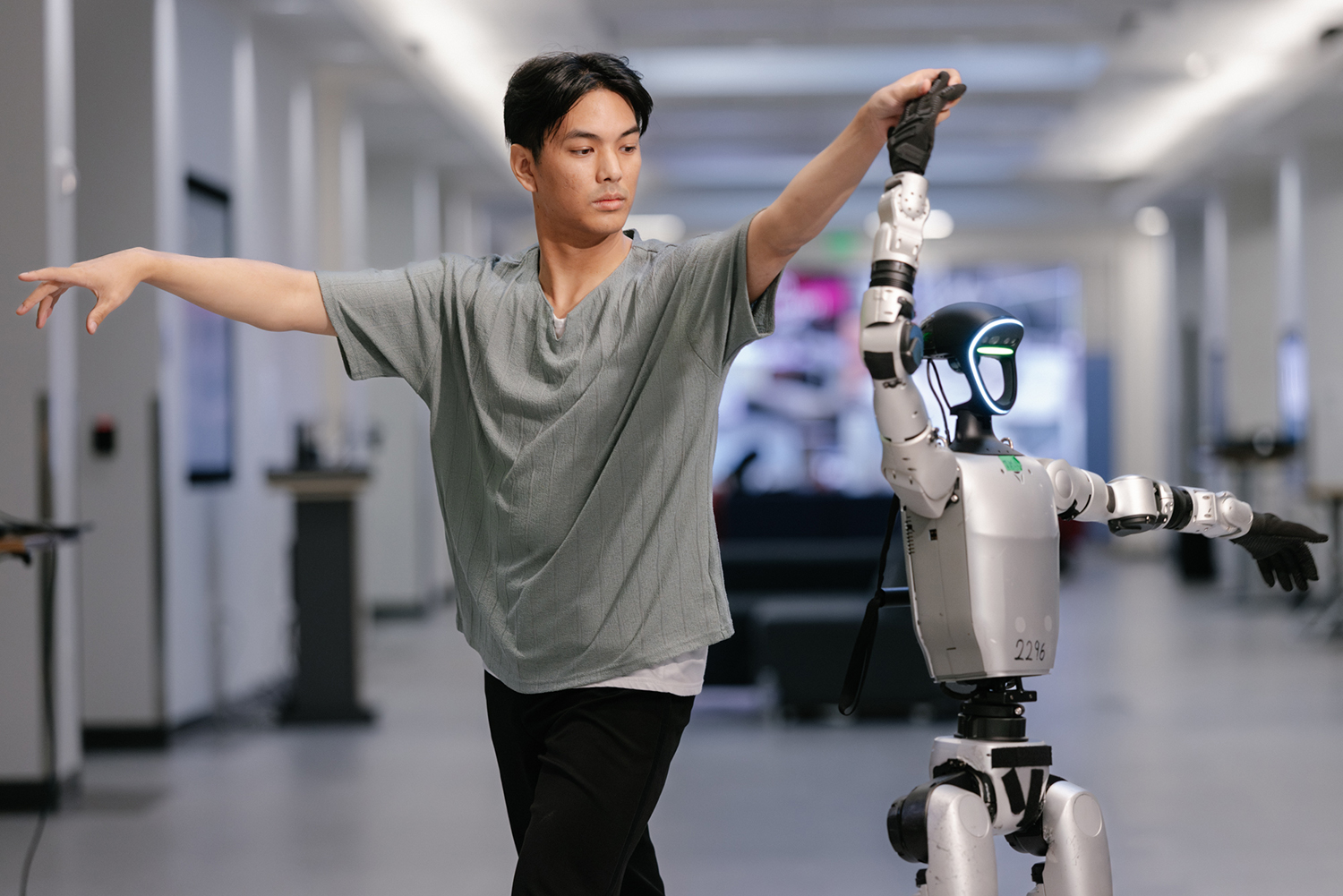A person dances with a humanoid robot, both extending their arms in a coordinated pose in a modern indoor space.