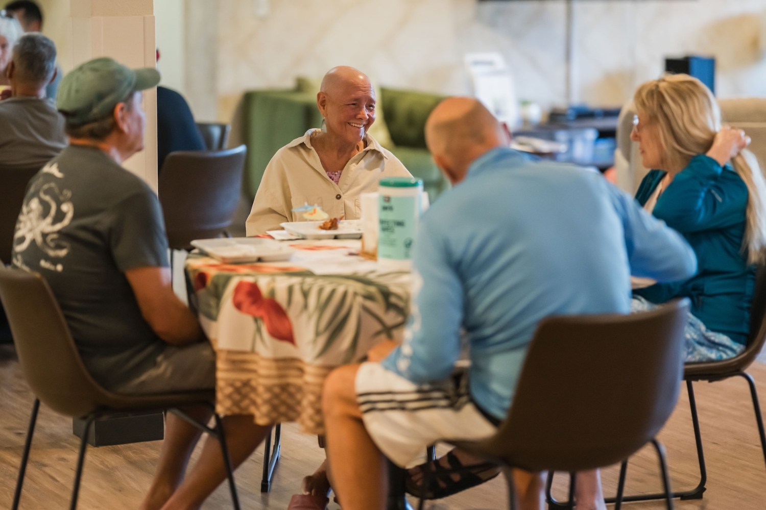 A group of four people sit around a table in a relaxed setting, engaged in conversation and sharing a meal together.