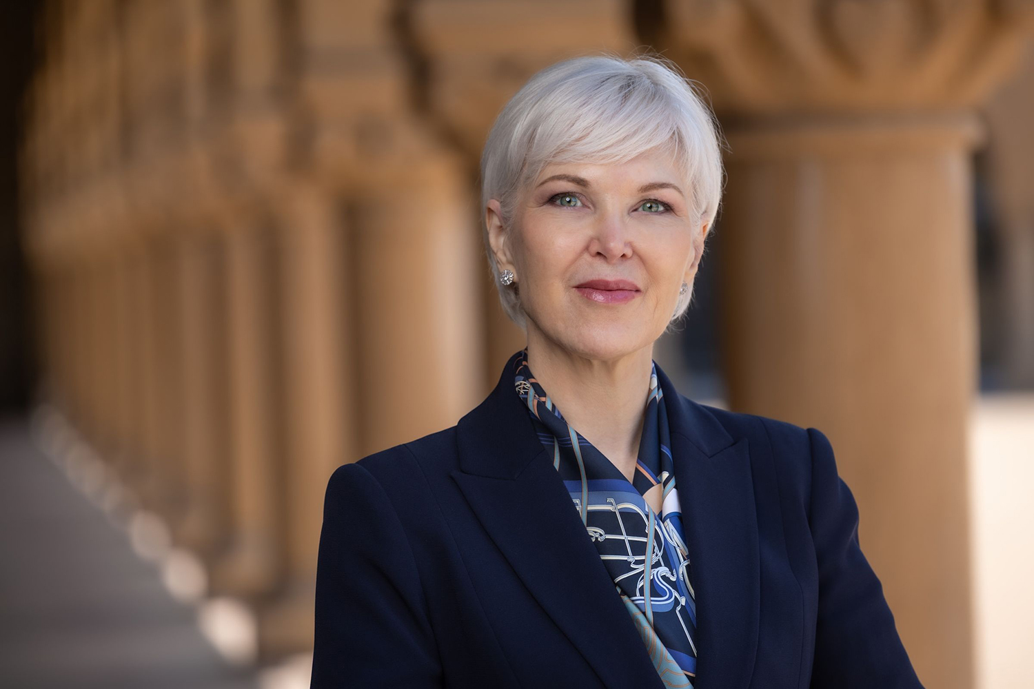 Professional headshot of Leanne Williams with short silver hair wearing a dark blazer and patterned scarf.
