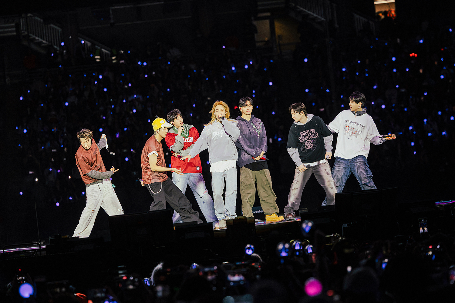 BTS dances energetically on stage, with colorful lighting and an enthusiastic crowd in the background.