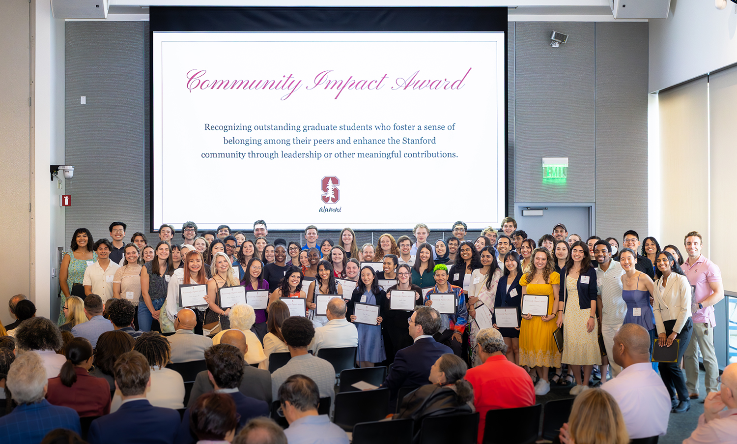 A large group of students stands together in a hall, holding certificates at an award ceremony celebrating their achievements.