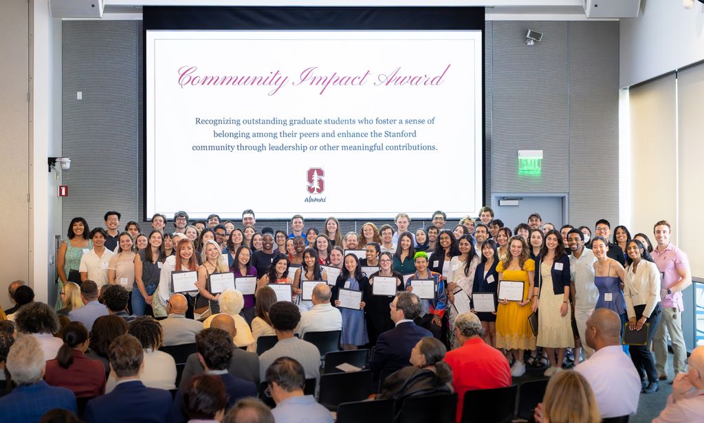A large group of students stands together in a hall, holding certificates at an award ceremony celebrating their achievements.