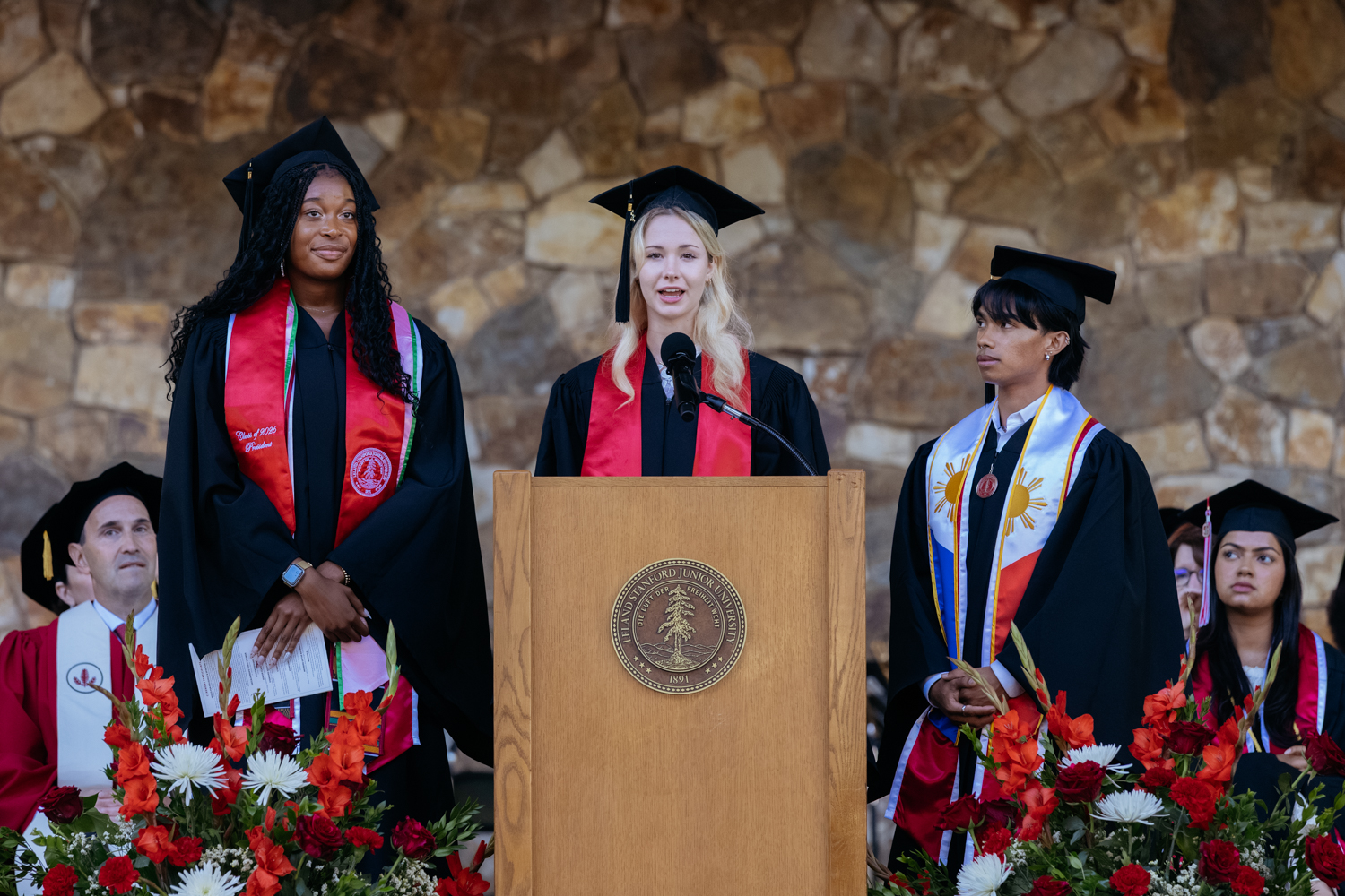 Graduates in caps and gowns stand at a podium, preparing to speak during Baccalaureate.