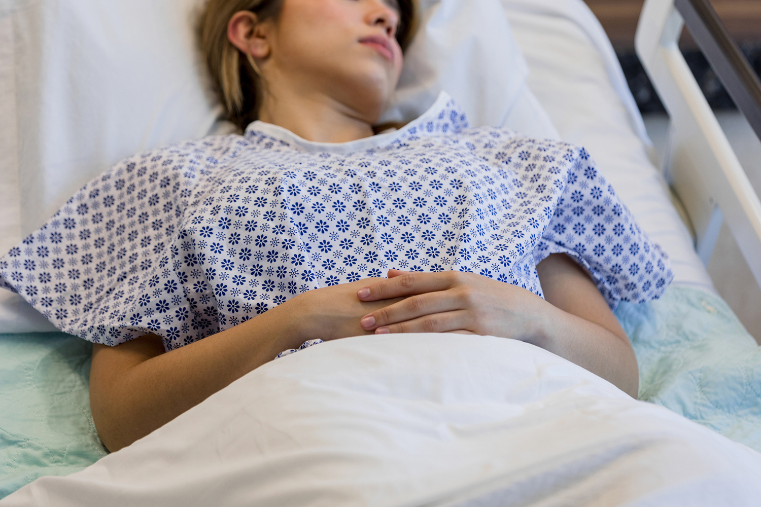 A patient lies in a hospital bed wearing a patterned gown.
