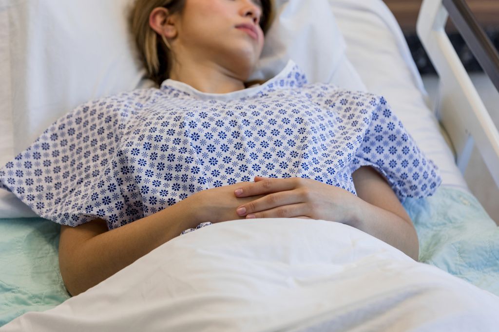 A patient lies in a hospital bed wearing a patterned gown.