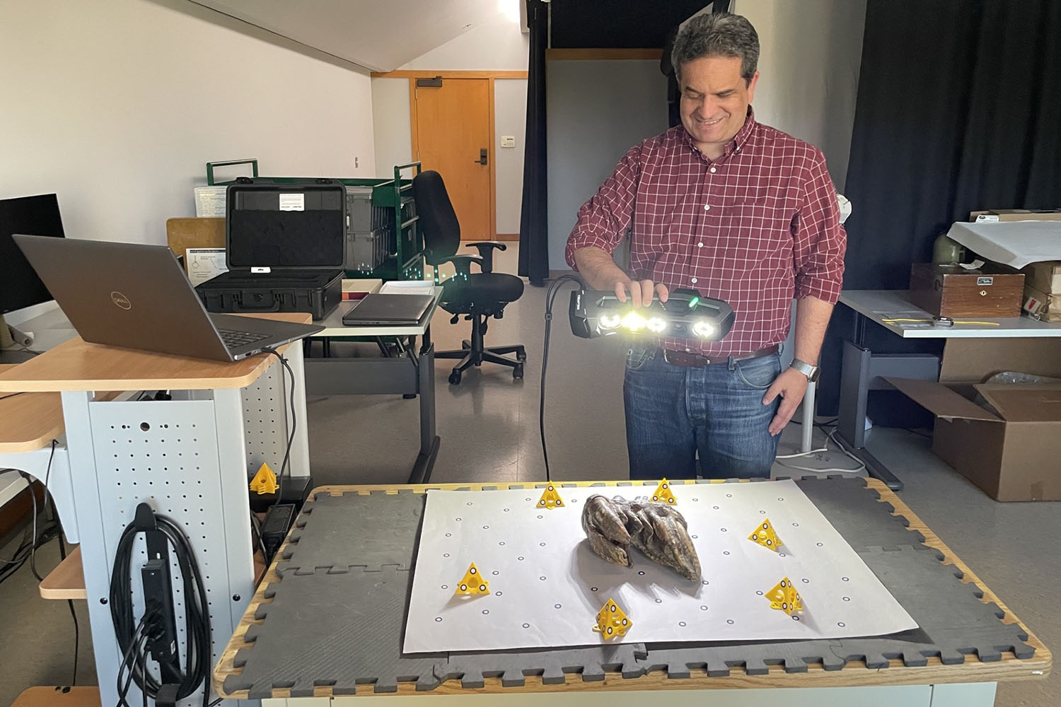 Tony Calavano smiling while scanning the fossil tooth with a handheld 3D scanner in a lab.