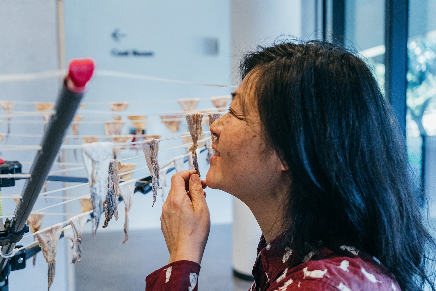 Patty Chang holds a piece of dried squid near her face beside a drying rack strung with more of them.