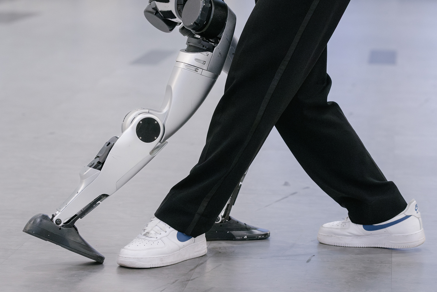A robotic leg moves alongside a person's foot wearing a white sneaker, showcasing advanced robotic movement.