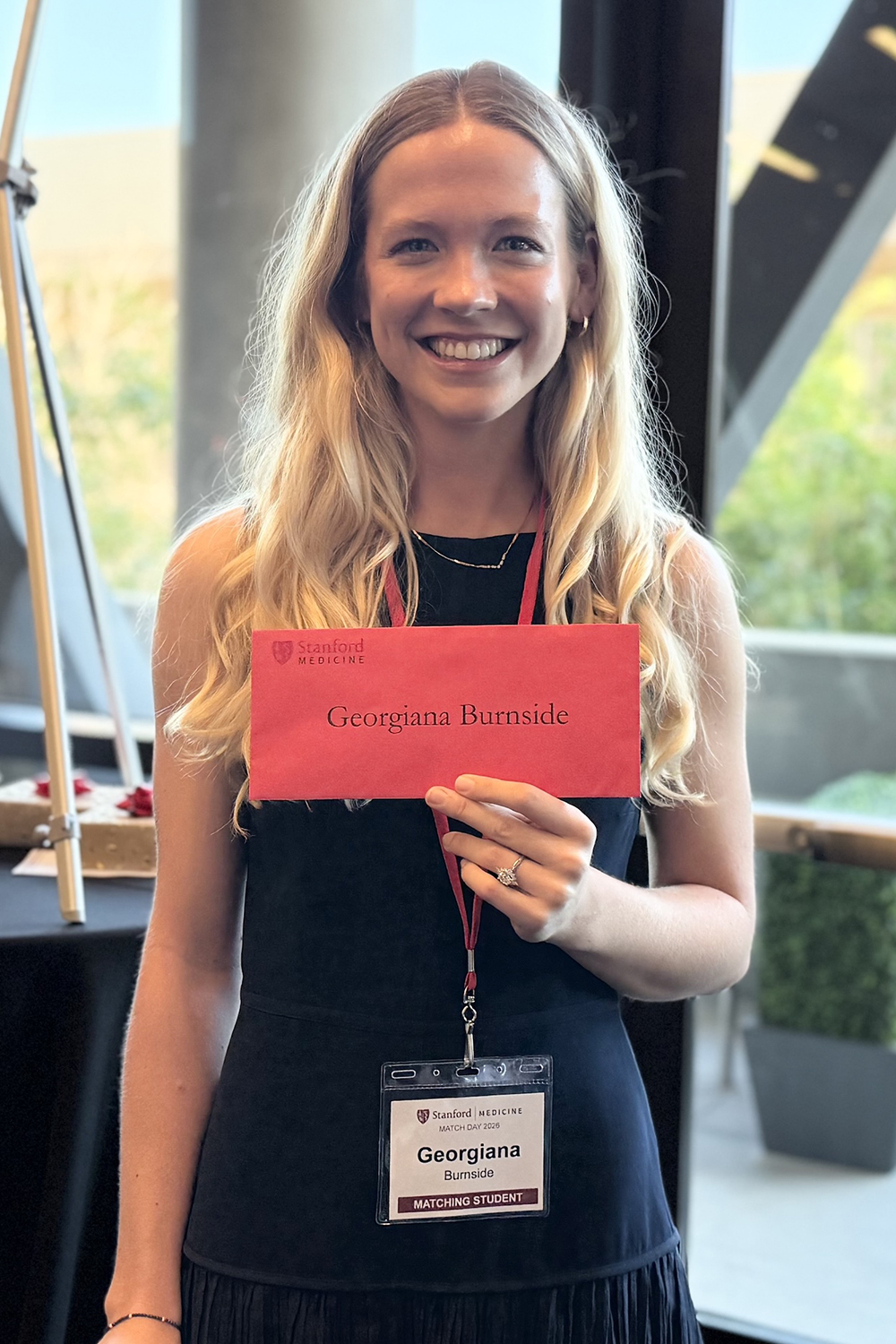 Georgiana Burnside poses for a photo while holding a red envelope with her name on it.