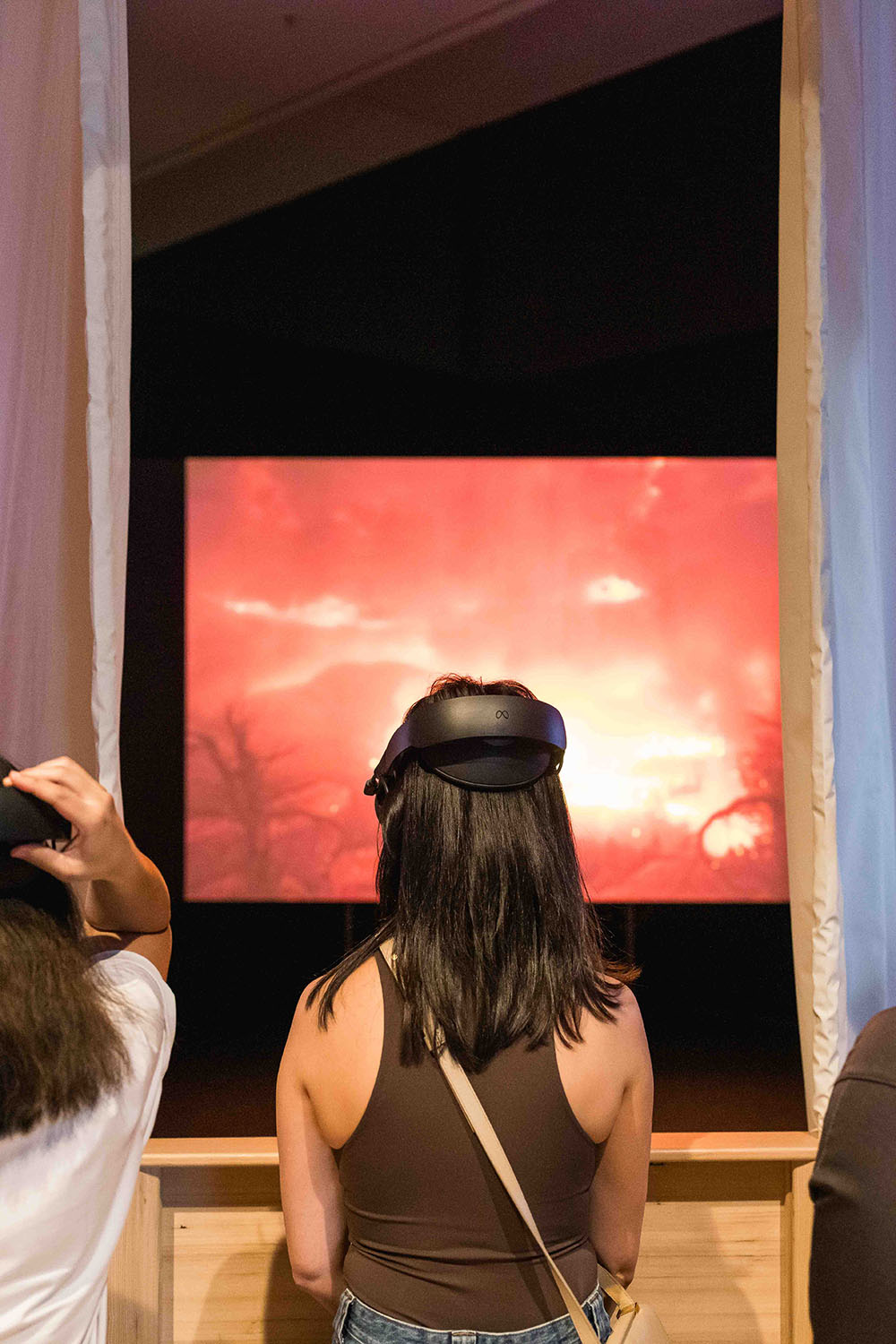 Visitor wearing a virtual reality headset views a fiery image on a screen in a gallery.