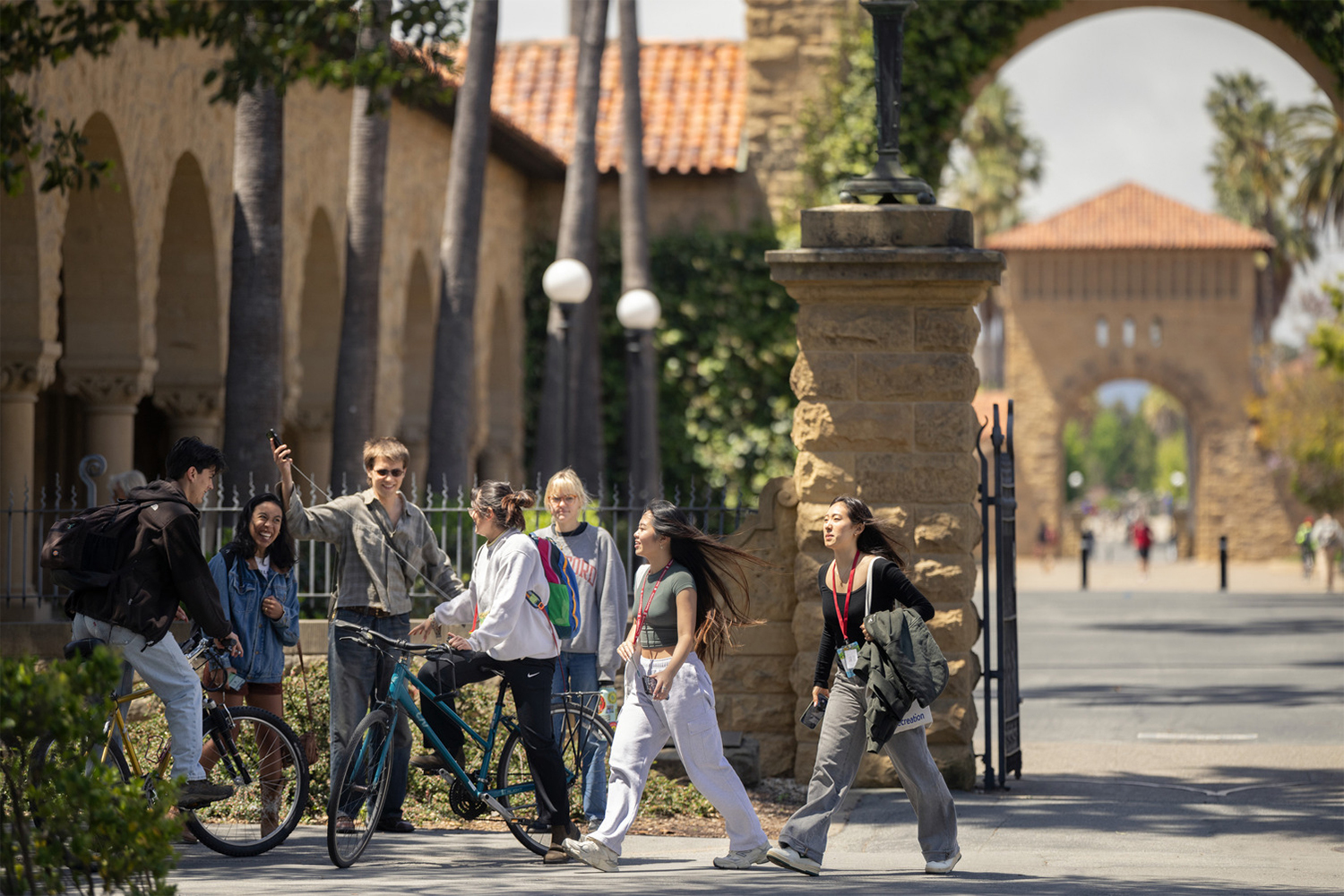 A group of students walk together on campus, engaging in conversation, with historic architecture and palm trees in the background.