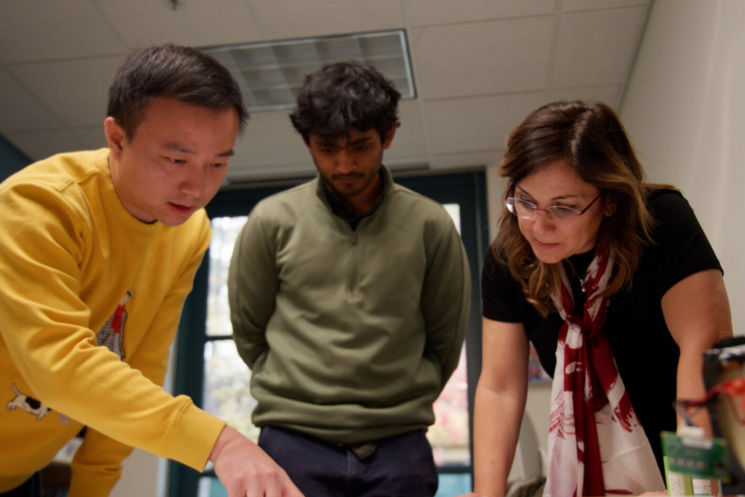 Three people collaborate around a table, discussing project details in an indoor workspace.