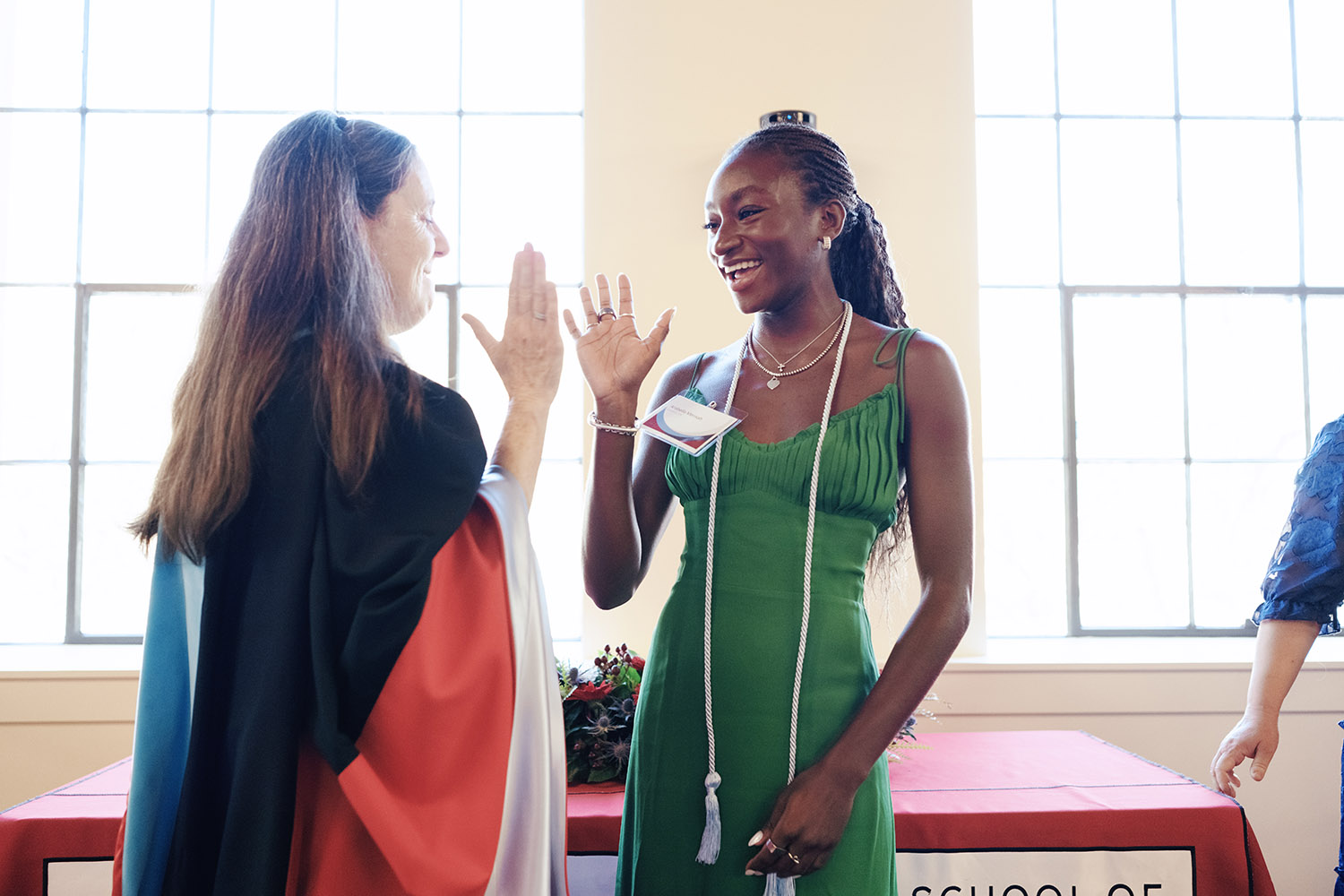 Undergraduate in a green dress raises her hand during the honor cord ceremony.
