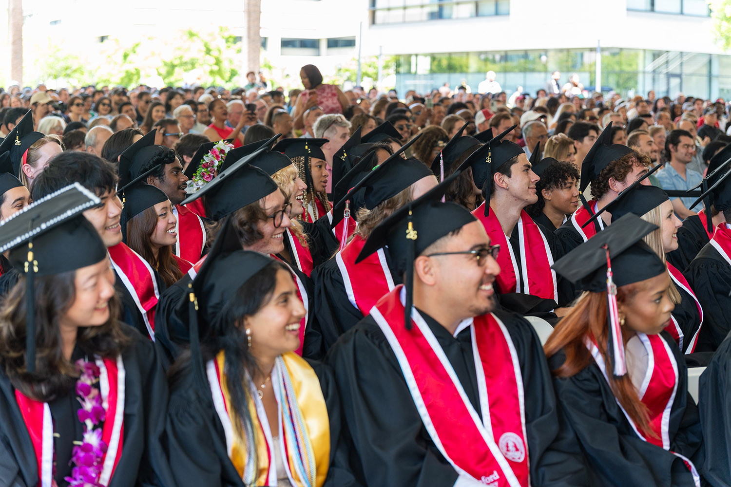 Graduation ceremony with attendees in caps and gowns, showcasing a large audience seated outdoors.