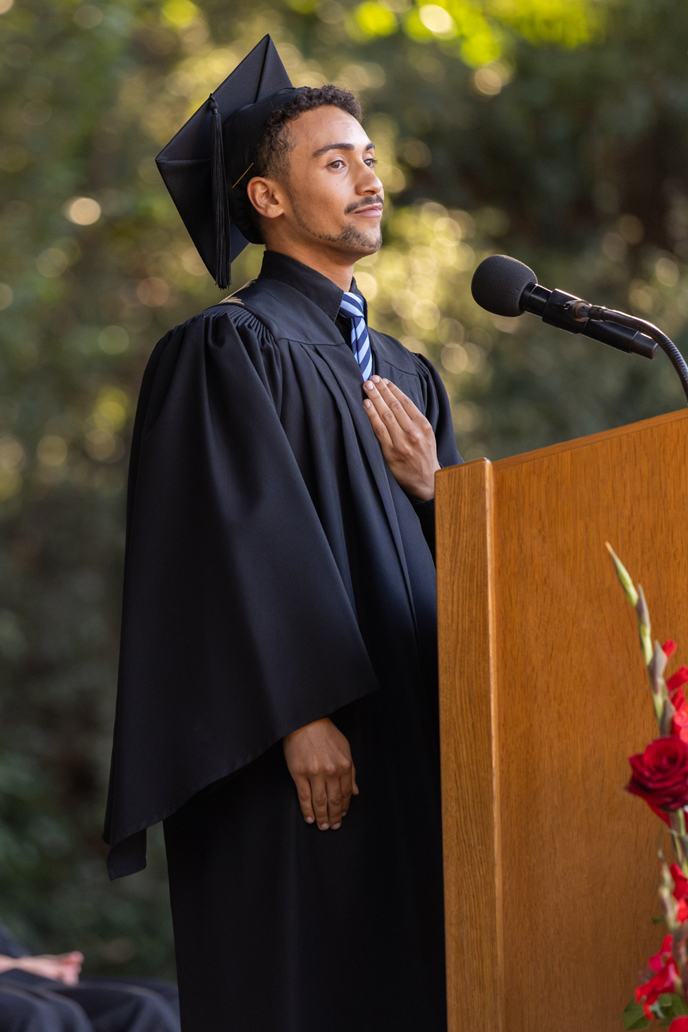 The student speaker places a hand over his heart while standing at a podium during Convocation.