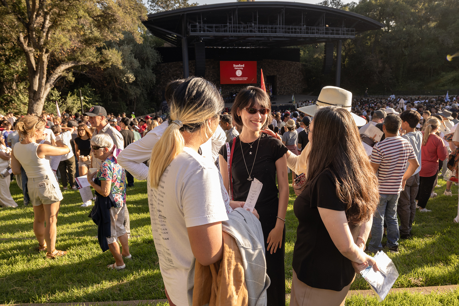 A group of people chat and smile together on the lawn near a stage during Convocation.