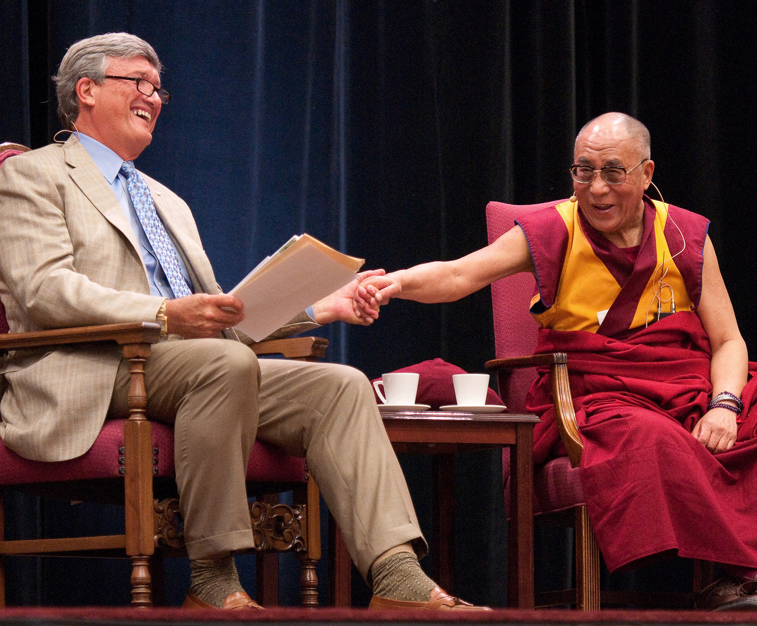 An image of James Doty and the Dalai Lama sitting on stage together at the Maples Pavilion in 2010.