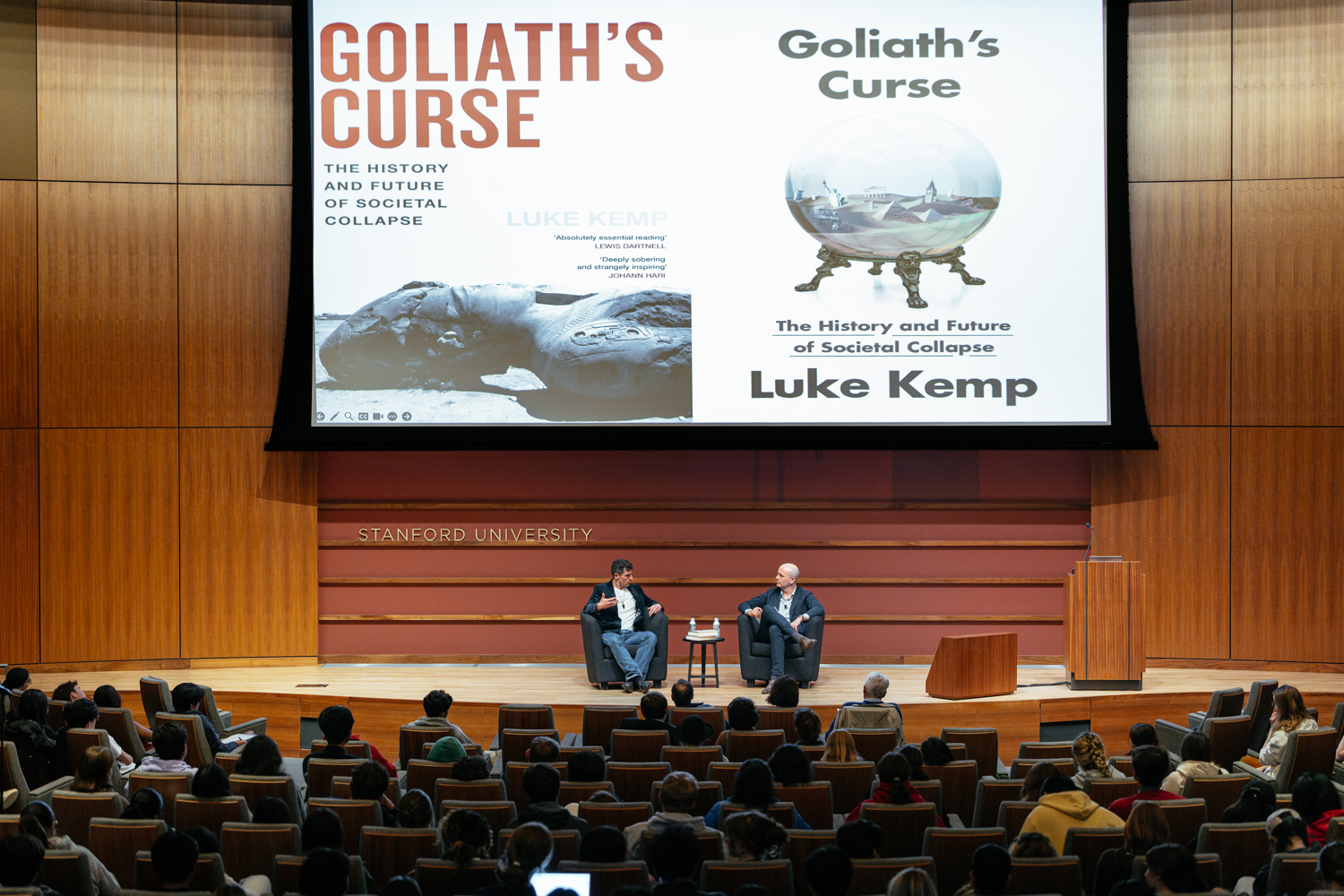 Wide shot of stage discussion of Luke Kemp's book Goliath's Curse about societal collapse at Stanford University.