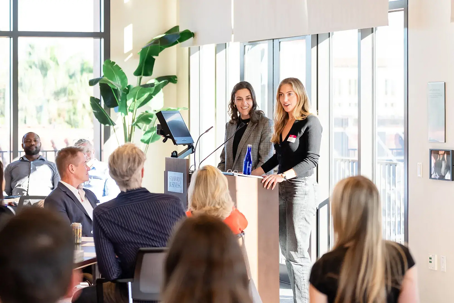 Sarah Strober  and Jenni Steiger speak at a podium during a presentation in front of an attentive audience.
