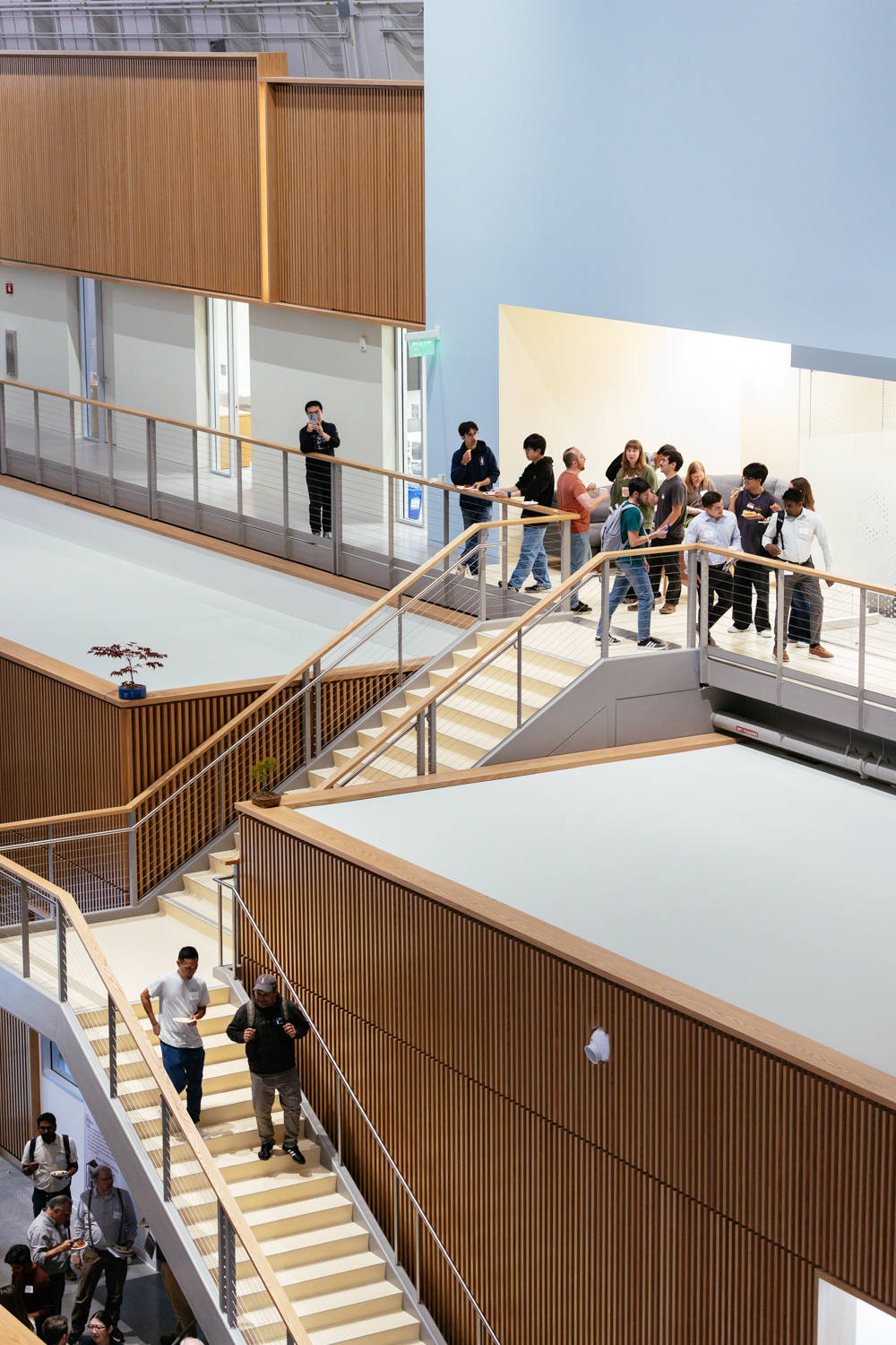 Students gather in a modern building, some on stairs and others standing, engaged with a drone flying above.