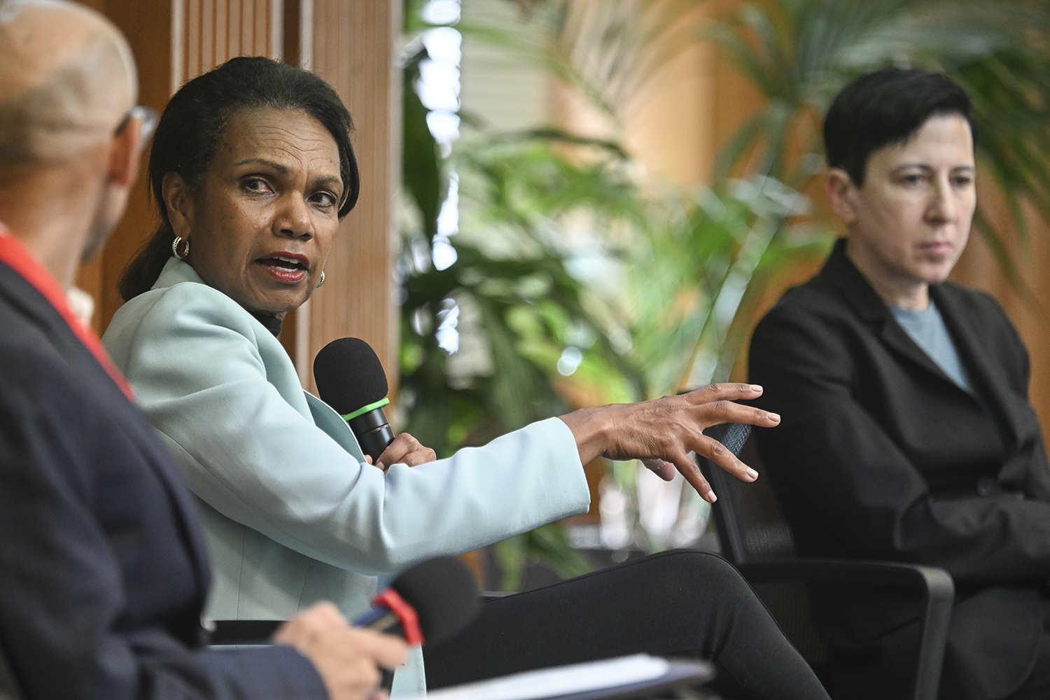 Condoleezza Rice gestures while speaking at a panel discussion, with two seated individuals visibly engaged in the conversation.