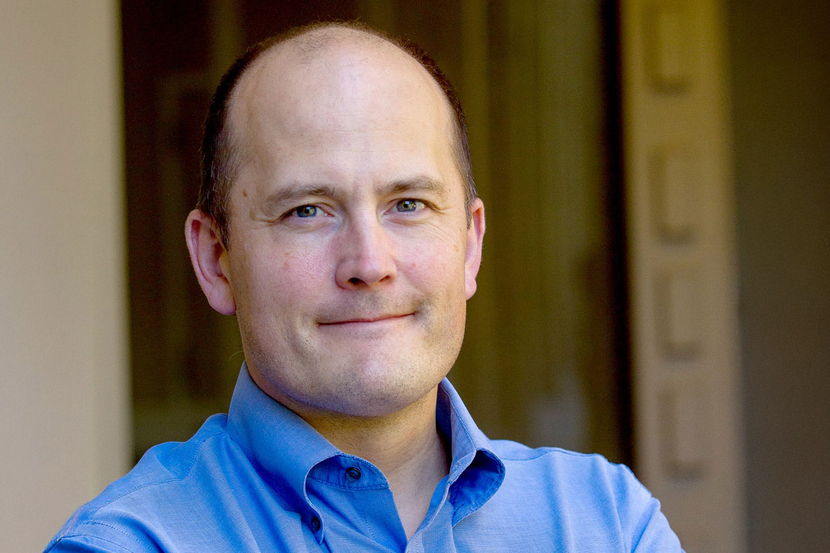Paul Bollyky headshot in blue shirt in outdoor setting.