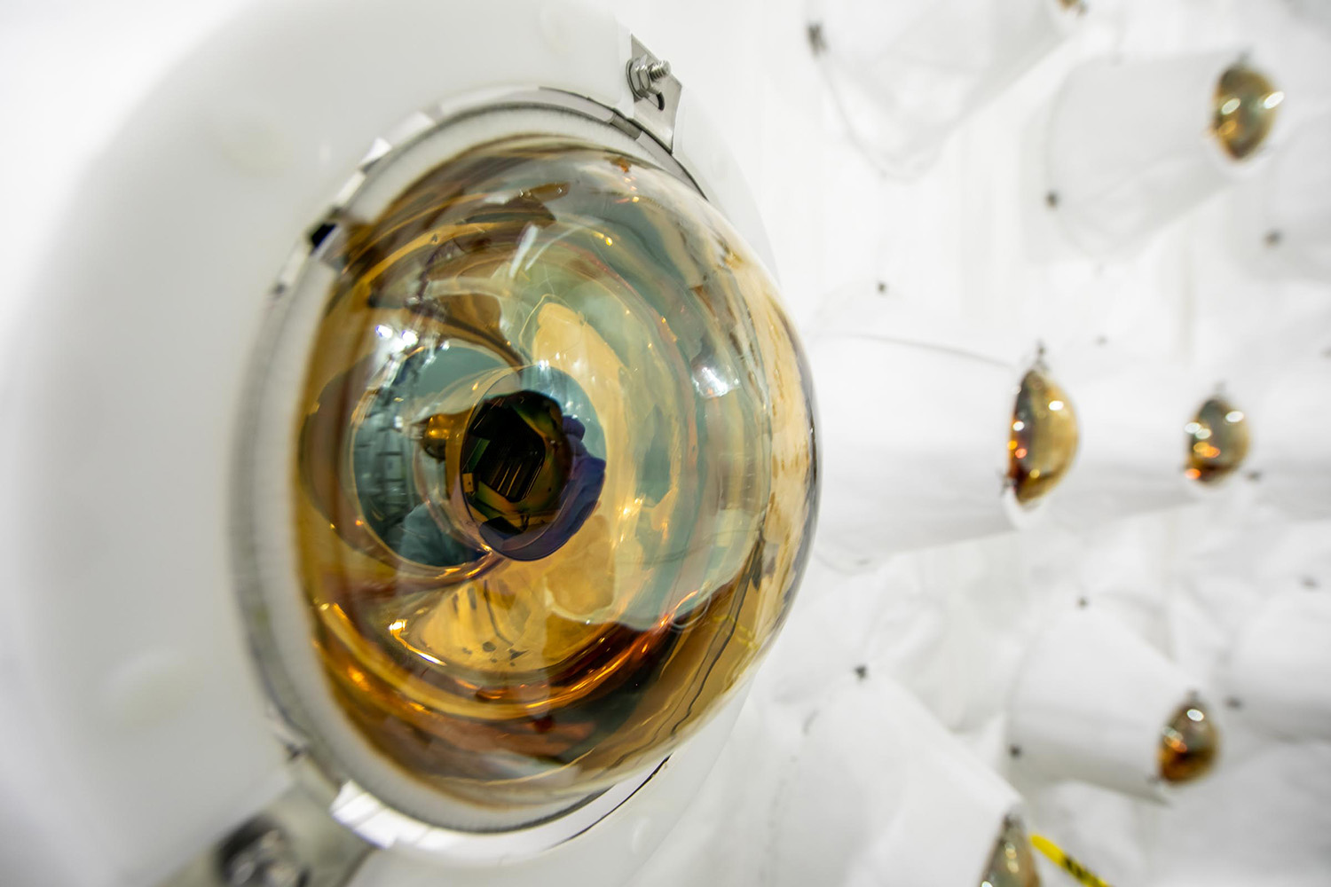 Close view of a gold-tinted dome-shaped light sensor mounted on a white detector wall, with others behind it.