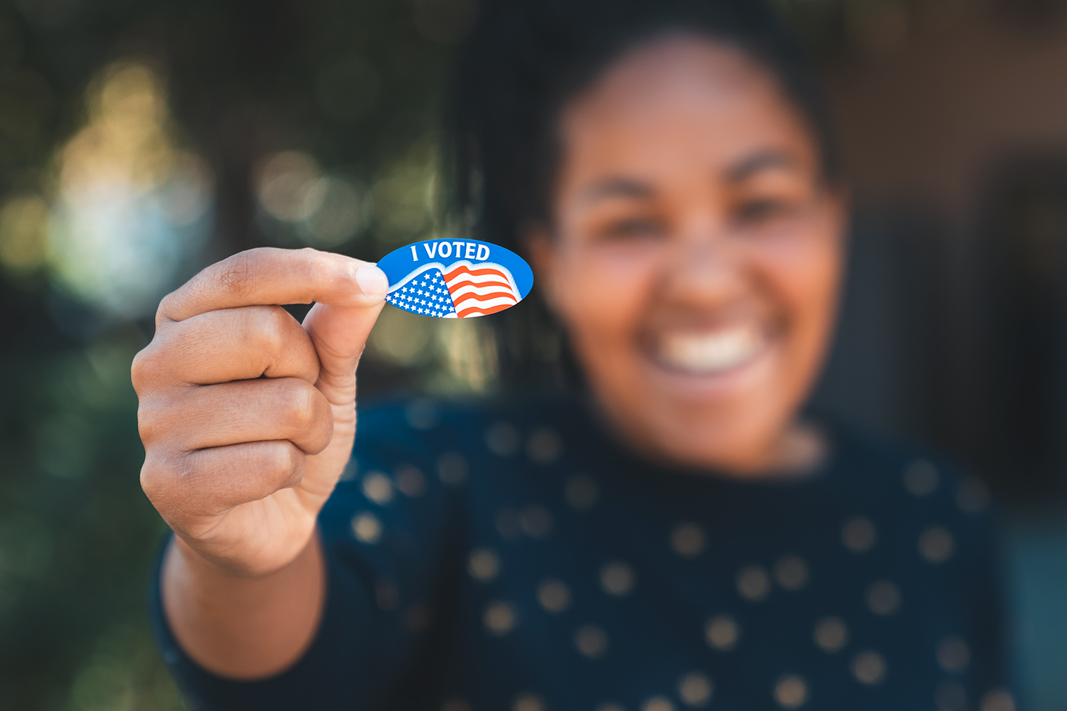 An image of a student holding out an I Voted sticker.