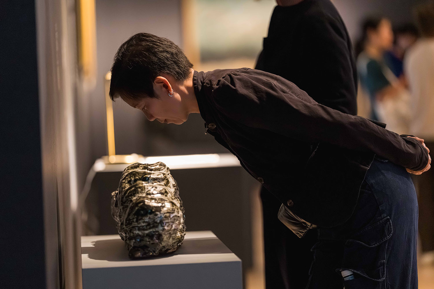 Visitor leans in to examine a textured sculpture displayed on a pedestal.
