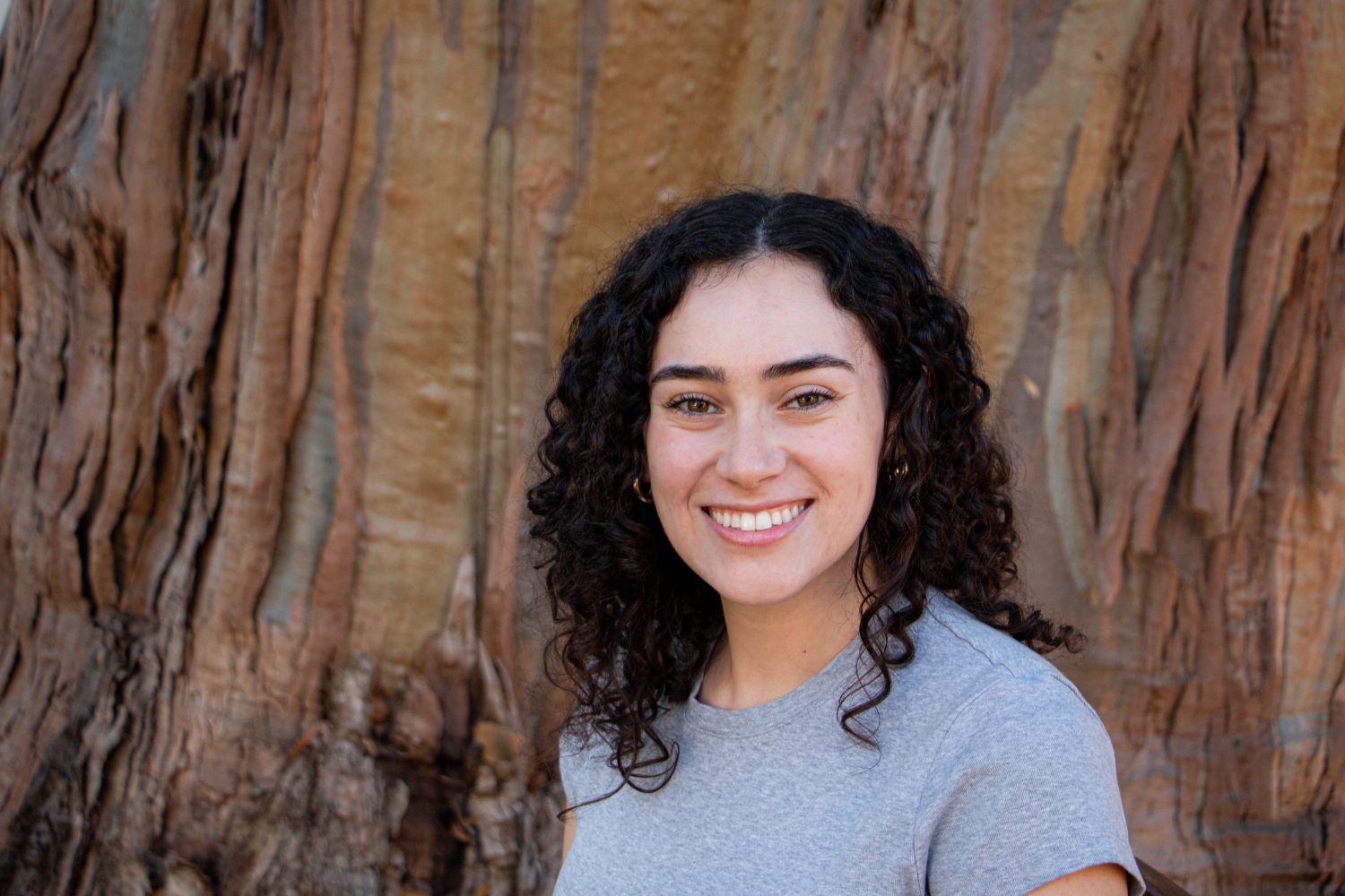 Angela Mata WIlliams posing in front of a tree's textured bark.